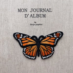 Pode incluir: Remendo de borboleta bordada com asas laranja e pretas, detalhes brancos e contorno preto. O remendo está em um fundo de tecido bege. O texto acima diz "MON JOURNAL D'ALBUM" e "by design graphics".