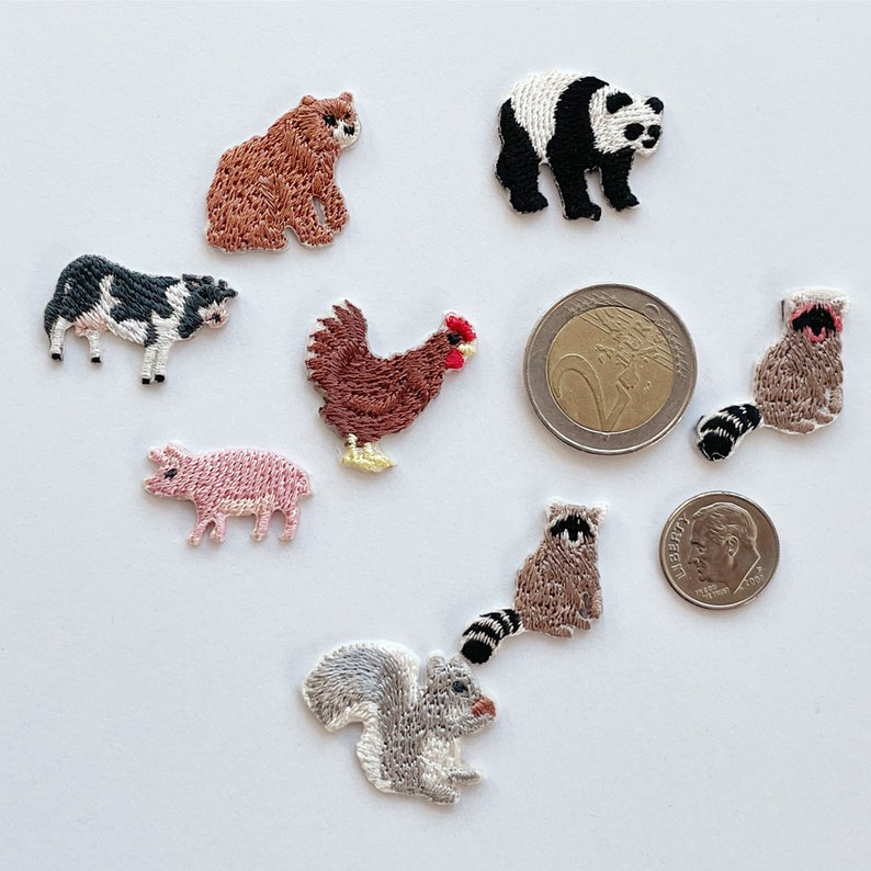 May include: Embroidered patches featuring various animals, including a bear, panda, cow, chicken, pig, raccoon, and squirrel. The patches are in various colors and sizes, with detailed stitching. A US dime and a Euro coin are included for size reference.