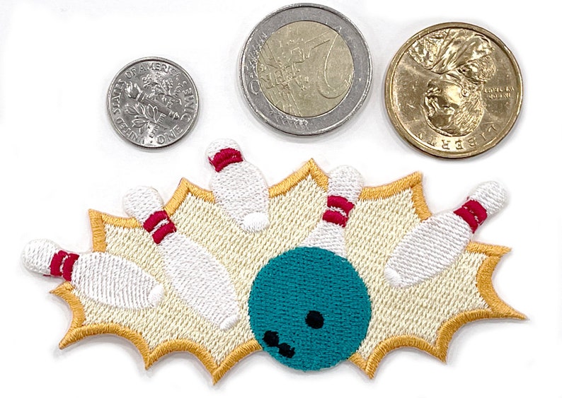 May include: Embroidered bowling patch featuring a teal bowling ball and white pins with red stripes, set against a beige background with a gold border. A dime, a Euro coin, and a dollar coin are also in the image.