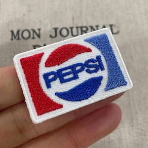 May include: Embroidered patch featuring the Pepsi logo. The patch is rectangular with a white border. The logo includes the word "PEPSI" in blue, with red and blue design elements. The patch is likely for clothing or accessories.