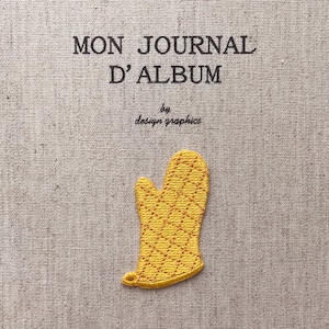 Op de afbeelding: Een gele geborduurde ovenwant patch met een ruitpatroon op een grijze stoffen achtergrond. De tekst "MON JOURNAL D'ALBUM" is in zwart boven de want geborduurd, met "by design graphics" eronder.