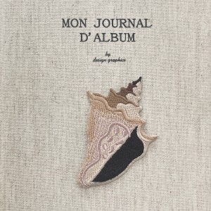 May include: A journal cover in beige fabric, featuring the text "MON JOURNAL D'ALBUM" and "by design graphics" in black. An embroidered seashell patch in beige, brown, black, and pink is attached to the cover.
