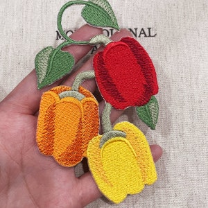 May include: Embroidered patch depicting three bell peppers in red, yellow, and orange. The peppers are linked by green stems and leaves. The patch is intricately stitched, displaying a botanical theme.