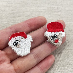 Op de afbeelding: Twee geborduurde Santa Claus gezicht patches. Elke patch heeft een rode hoed, witte baard en een lachend gezicht met zwarte ogen en een rode neus. Ideaal voor vakantie-thema ambachten.