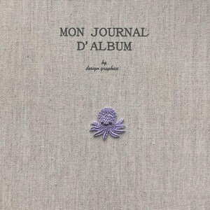 Pu&ograve; includere: Una copertina di album in tessuto grigio chiaro con la scritta "MON JOURNAL D'ALBUM" e "by design graphics" stampata in nero. Un piccolo polpo viola ricamato &egrave; centrato in basso. La copertina dell'album ha un aspetto strutturato.