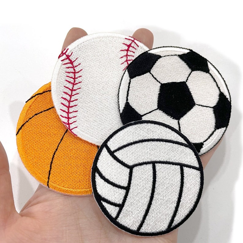 May include: Four embroidered patches depicting sports balls: a baseball with red stitching, a basketball with orange texture, a football with black and white pentagons, and a volleyball with white lines.