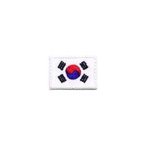 May include: A small, rectangular patch featuring the South Korean flag. The flag has a white background with a red and blue Taegeuk in the center, surrounded by four black trigrams in each corner. The patch is bordered by a white stitched edge.
