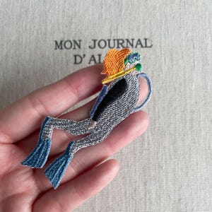 Op de afbeelding: Geborduurde patch van een duiker in zittende positie, met een grijs pak, blauwe vinnen en een oranje en gele helm. De patch wordt in een hand gehouden, met de tekst "MON JOURNAL D'AI" zichtbaar op de achtergrond.