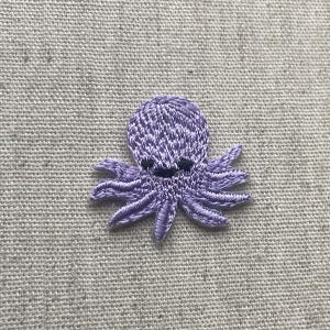 Pu&ograve; includere: Una piccola toppa ricamata a forma di polpo nei toni del lavanda e del bianco. Il polpo ha un volto sorridente e otto tentacoli dettagliati. La toppa &egrave; probabilmente progettata per essere cucita su tessuto, aggiungendo un elemento decorativo.