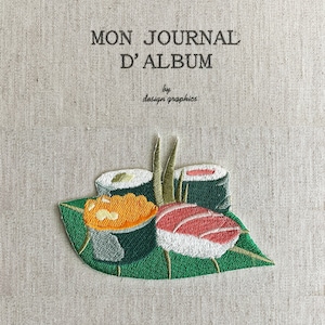 Peut inclure: Couverture de journal brodée avec le texte "MON JOURNAL D'ALBUM" et un motif de sushi. Le sushi comprend des rouleaux et des nigiris sur une feuille verte. La couverture est de couleur beige neutre.