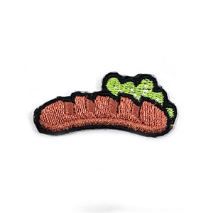 Könnte beinhalten: Gestickter Aufnäher mit einem braunen Hotdog mit grünem Relish, schwarz umrandet. Der Aufnäher ist zum Aufbügeln oder Aufnähen auf Stoff konzipiert. Ideal, um Kleidung oder Accessoires einen Hauch von Spaß zu verleihen.