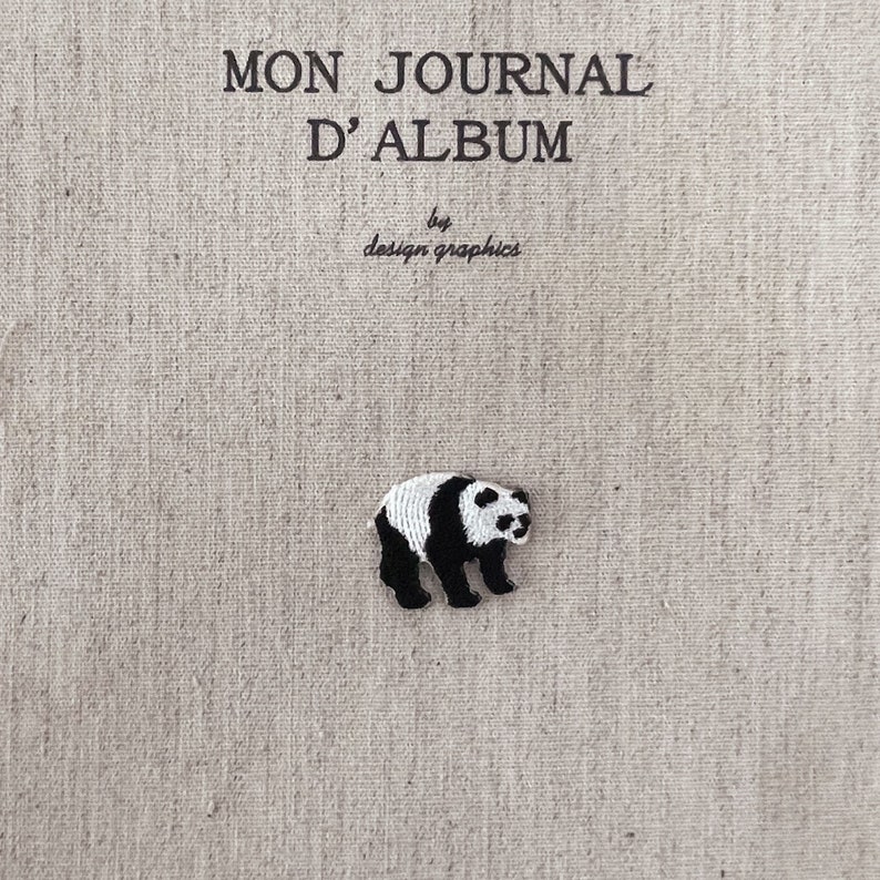 May include: A small, embroidered panda bear patch in black and white, placed on a beige linen background. The text "MON JOURNAL D'ALBUM" and "by design graphics" are printed in black above the panda.