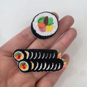 Puede incluir: Parches de sushi bordados. Uno es una pieza redonda y el otro un rollo. Ambos tienen un borde negro y arroz blanco. Los rellenos son coloridos: naranja, verde, rosa y amarillo. Ideal para añadir a ropa o accesorios.