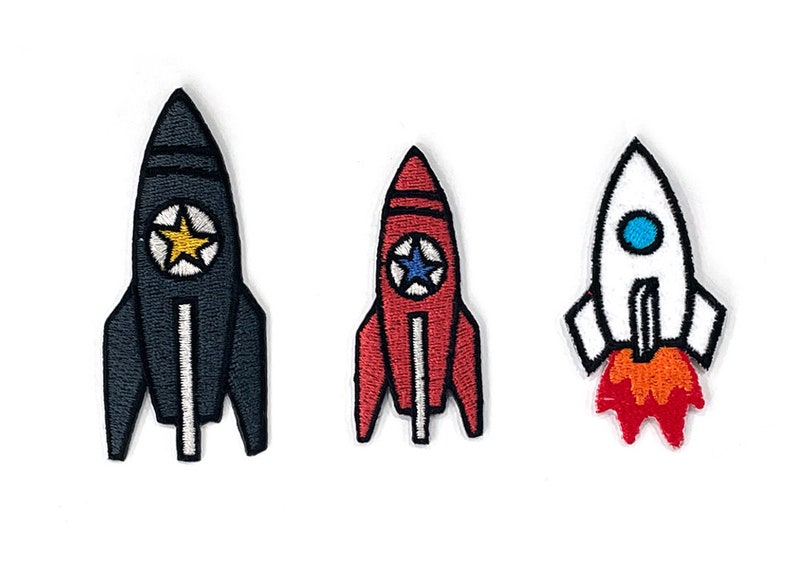 May include: Three embroidered rocket ship patches in black, red, and white. The black rocket has a yellow star, the red rocket has a blue star, and the white rocket has a blue circle and orange flames.
