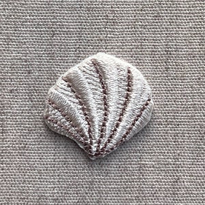 K&ouml;nnte beinhalten: Ein kleiner, gestickter Muschel-Aufn&auml;her in Wei&szlig;- und Hellbraunt&ouml;nen. Der Aufn&auml;her weist detaillierte Stiche auf, die die Form und die Rippen der Muschel umrei&szlig;en. Der Aufn&auml;her dient wahrscheinlich dekorativen Zwecken.