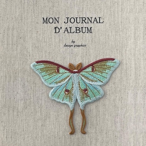 May include: Embroidered patch featuring a Luna moth with teal, brown, and red details. The moth is centered on a beige fabric background. The text "MON JOURNAL D'ALBUM" is printed above the moth, with "by design graphics" below.