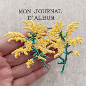 May include: Embroidered yellow floral applique with green stems. The applique features detailed stitching and a delicate design, perfect for embellishing clothing or crafts. The background includes the text "MON JOURNAL D'ALBUM".
