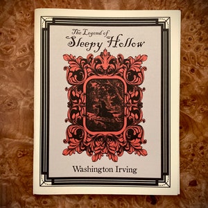 K&ouml;nnte beinhalten: Buchcover f&uuml;r "The Legend of Sleepy Hollow" von Washington Irving. Das Cover zeigt einen dekorativen korallenfarbenen Rahmen mit schwarzen Akzenten, ein zentrales Bild und Text. Der Hintergrund ist hellgrau.