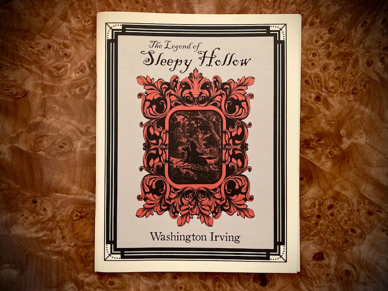 K&ouml;nnte beinhalten: Buchcover f&uuml;r "The Legend of Sleepy Hollow" von Washington Irving. Das Cover zeigt einen dekorativen korallenfarbenen Rahmen mit schwarzen Akzenten, ein zentrales Bild und Text. Der Hintergrund ist hellgrau.