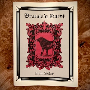 May include: A book cover with a black and white illustration of a wolf in a red frame with ornate black details. The title is "Dracula's Guest" and the author is "Bram Stoker".