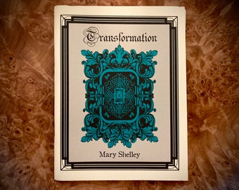 Könnte beinhalten: Ein Buchcover mit einem schwarzen und weißen Rahmen und einem verzierten Design in Tealblau und Schwarz. Der Titel "Transformation" ist in einer dekorativen Schrift geschrieben. Der Autor "Mary Shelley" steht unter dem Design.