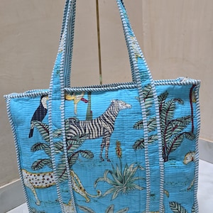 May include: A large, light blue tote bag with a quilted design. The bag features a vibrant jungle scene with zebras, leopards, and toucans. The handles and edges are trimmed with a white and blue striped fabric.