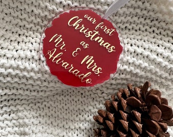 May include: Red round Christmas ornament with gold lettering that reads "our first Christmas as Mr. & Mrs. Alvarado".