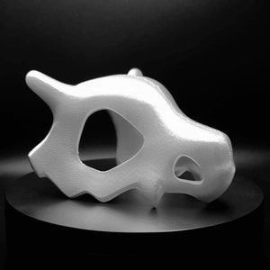 May include: A white 3D printed model of a Pokemon skull. The skull is detailed and has a smooth, glossy finish.