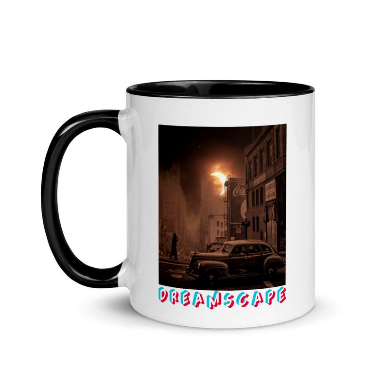 May include: White ceramic mug with a black interior and handle. The mug features a vintage-style image of a city street scene with a classic car and the text "DREAMSCAPE" in red and blue. A Coca-Cola sign is visible.