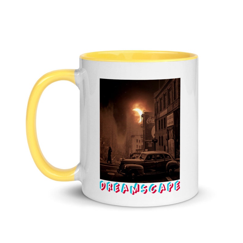May include: White ceramic mug with a yellow handle and interior. The mug features a vintage cityscape scene with a classic car, a person walking, and the word "DREAMSCAPE" in colorful text. The mug is designed for hot beverages.