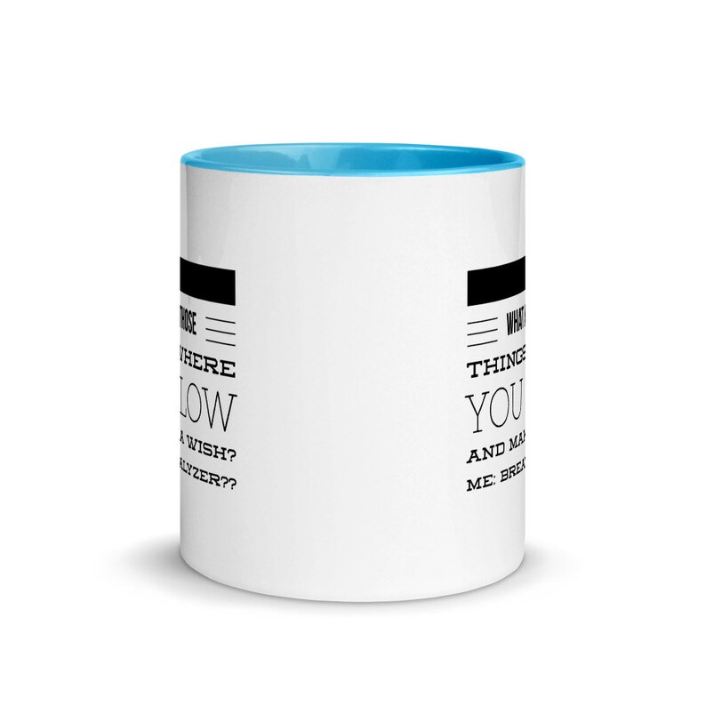 May include: White ceramic coffee mug with a light blue interior. The mug features black text on both sides. One side reads "Where do wishes flow?" and the other side reads "What things make you..."