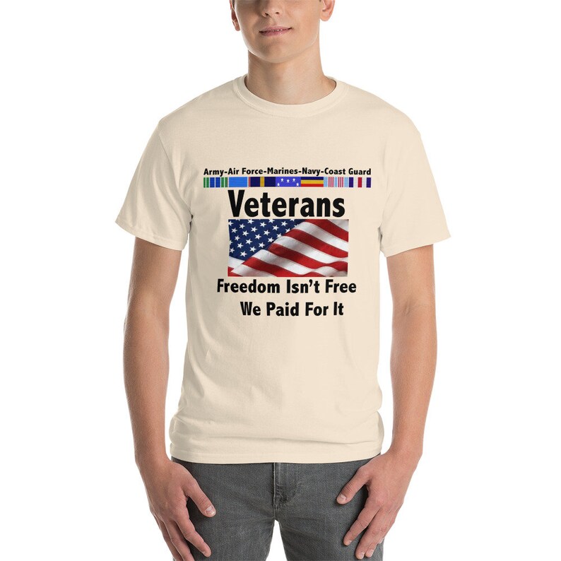 May include: Cream-colored t-shirt featuring the text "Veterans" above an American flag graphic. Below the flag, the text reads "Freedom Isn't Free, We Paid For It." Above the word "Veterans" are service ribbons.