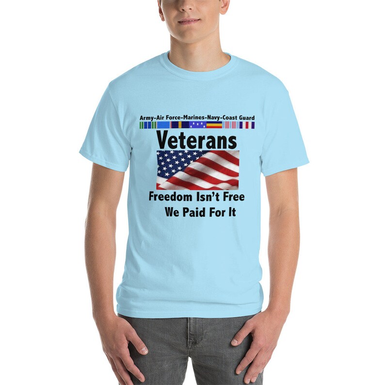 May include: Light blue t-shirt with the text "Veterans" above a waving American flag. The shirt also features the text "Freedom Isn't Free, We Paid For It" and the names of the military branches.