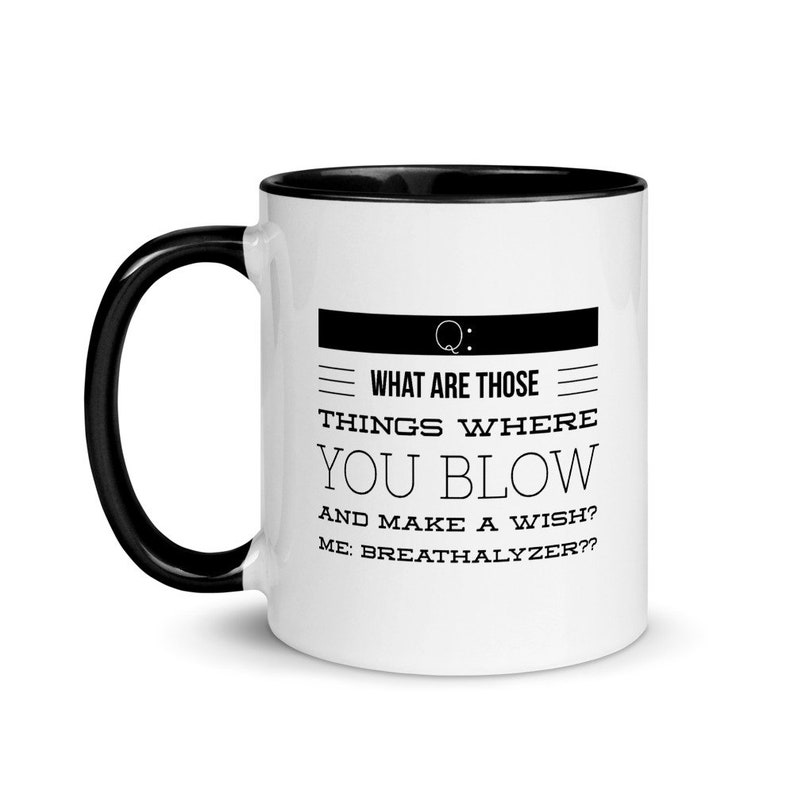 May include: White ceramic coffee mug with a black handle and interior. The mug features the text "WHAT ARE THOSE THINGS WHERE YOU BLOW AND MAKE A WISH? ME: BREATHALYZER??" in black font.