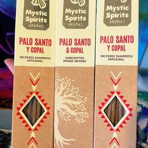 May include: Three incense packages labeled "Mystic Spirits Aromas" with "Palo Santo Y Copal" and "Palo Santo & Copal". The packages are tan with red and white geometric designs and text. One package says "Handcrafted Smudge Incense".