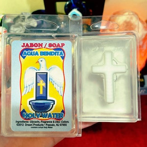 May include: A clear plastic package containing a white soap bar with a white cross on top. The soap bar is labeled "Jabon/Soap Agua Bendita Holy Water" and includes the ingredients and copyright information.