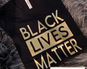 May include: Black t-shirt with gold lettering that reads "Black Lives Matter".