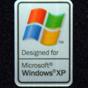 May include: A rectangular sticker with a white border displays the Windows logo in red, green, blue, and yellow. The text below reads "Designed for Microsoft Windows XP."
