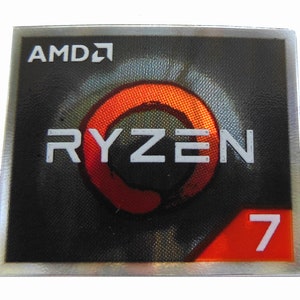 May include: A square sticker with a silver border. The AMD logo is at the top, with the word "RYZEN" below it. A red and orange circular design is behind the word. The number "7" is in a red rectangle at the bottom.