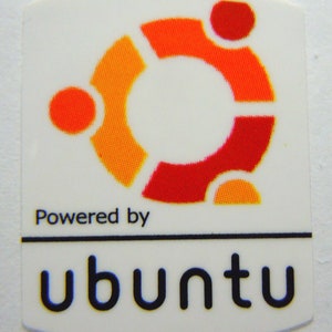 May include: White sticker featuring the Ubuntu logo, a stylized orange and red circle design. Below the logo, the text reads "Powered by" above the word "ubuntu" in black, bold font. The sticker has rounded corners.