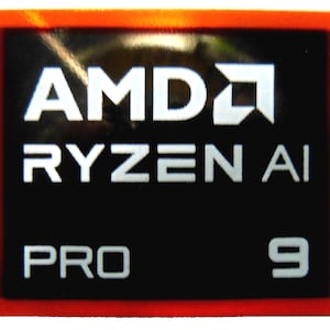 Pu&ograve; includere: Un adesivo rettangolare con bordo arancione e centro nero. L'adesivo presenta il testo bianco "AMD", "RYZEN AI", "PRO" e il numero "9". Il logo AMD &egrave; anch'esso bianco.