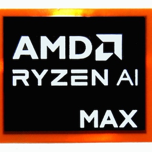 May include: A rectangular sticker with an orange border and a black center. The white text reads "AMD RYZEN AI MAX". The AMD logo is also white. The sticker is likely for a computer component.