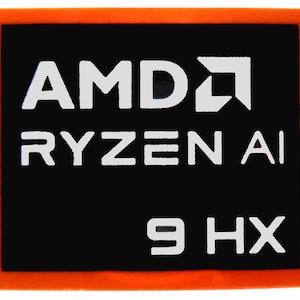 Puede incluir: Un parche rectangular con borde naranja y centro negro. El texto blanco dice "AMD RYZEN AI 9 HX". El logotipo de AMD también es blanco. El parche es probablemente para un componente de computadora.