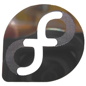 Op de afbeelding: Een metallic, druppelvormig embleem met een grote, witte letter "f" uitgesneden. Het embleem heeft een reflecterend, donkergrijs oppervlak met een gestructureerd, zilverkleurig patroon op de bovenste linkerkromming van de "f".