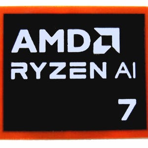 Op de afbeelding: Een rechthoekige patch met een oranje rand en een zwart midden. De witte tekst luidt "AMD RYZEN AI 7". Het AMD-logo is ook wit en bevindt zich in de linkerbovenhoek van de patch.