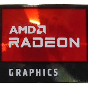 Puede incluir: Una pegatina rectangular con fondo rojo y texto blanco. El texto dice "AMD RADEON GRAPHICS". El logotipo de AMD es visible en la esquina superior izquierda. La pegatina tiene un borde negro.