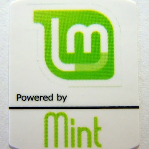 Könnte beinhalten: Ein weißer Aufkleber mit einem grünen Linux Mint Logo und dem Text "Powered by Mint".