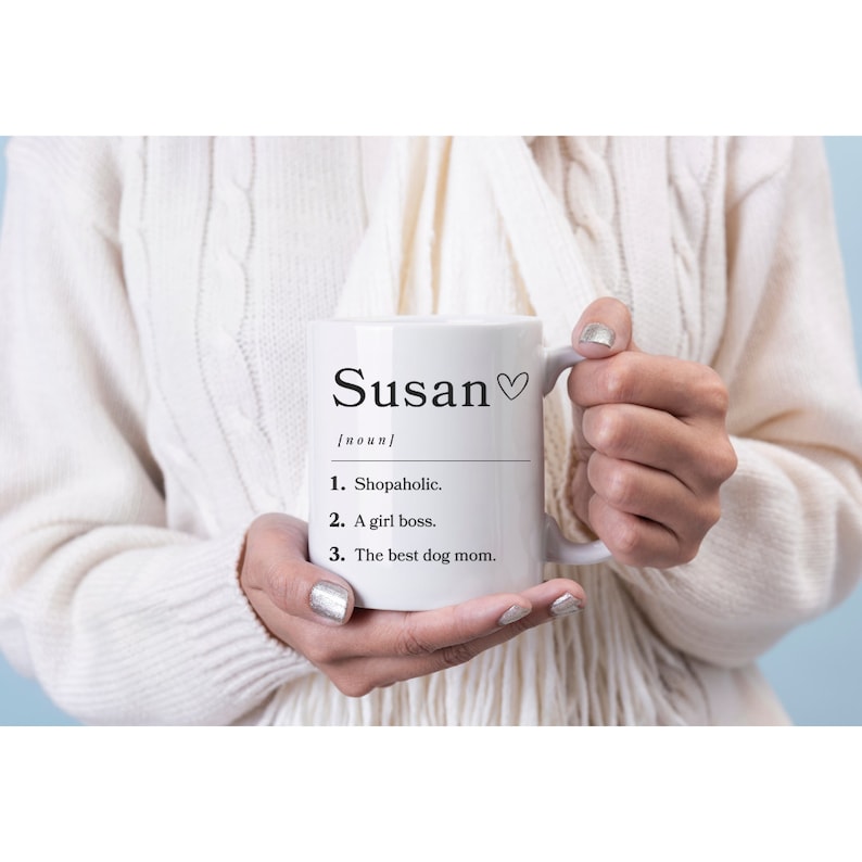 K&ouml;nnte beinhalten: Wei&szlig;e Keramiktasse mit einer schwarzen Aufschrift, die lautet: "Susan [Substantiv] 1. Shopaholic. 2. Eine Chefin. 3. Die beste Hundefreundin."