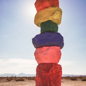Puede incluir: Una pila de rocas coloridas pintadas de rojo, amarillo, verde, azul, rosa y rojo, de pie en un paisaje desértico.
