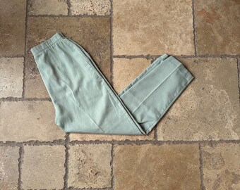 May include: A pair of light green pants folded in half on a tiled floor.